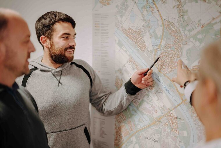 Drei Personen stehen um eine Karte herum, eine zeigt mit einem Stift auf die Karte
