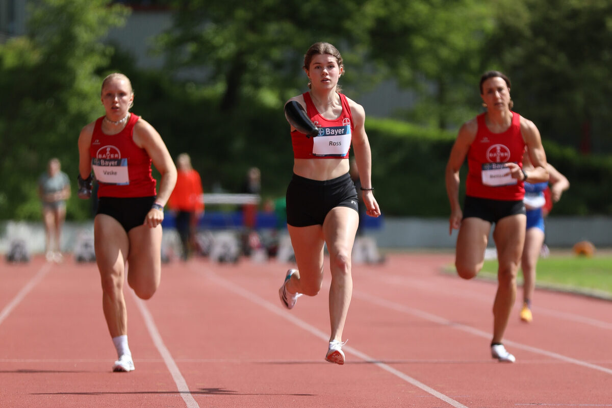 Drei Personen mit körperlichen Beeinträchtigungen laufen auf einem Sportplatz