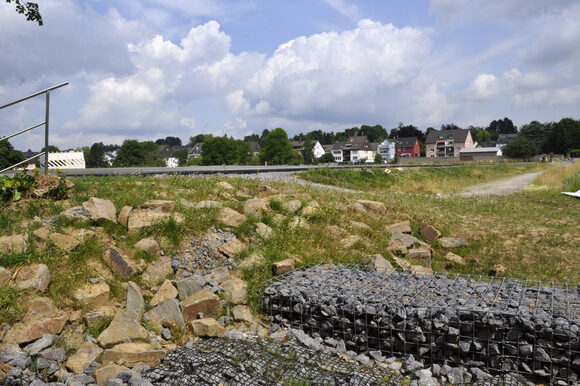 Der Deich schiebt sich zwischen Dhünn und Odenthaler Straße vor den Ortsteil Schlebusch (Gabionenwand im Vordergrund)