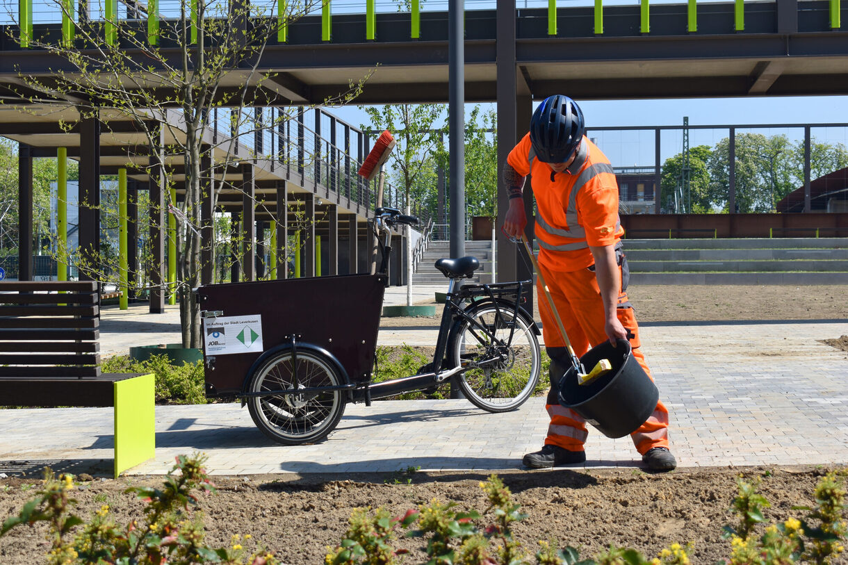Ein Mitarbeiter des Job Services sammelt Müll im Brückenpark Opladen ein