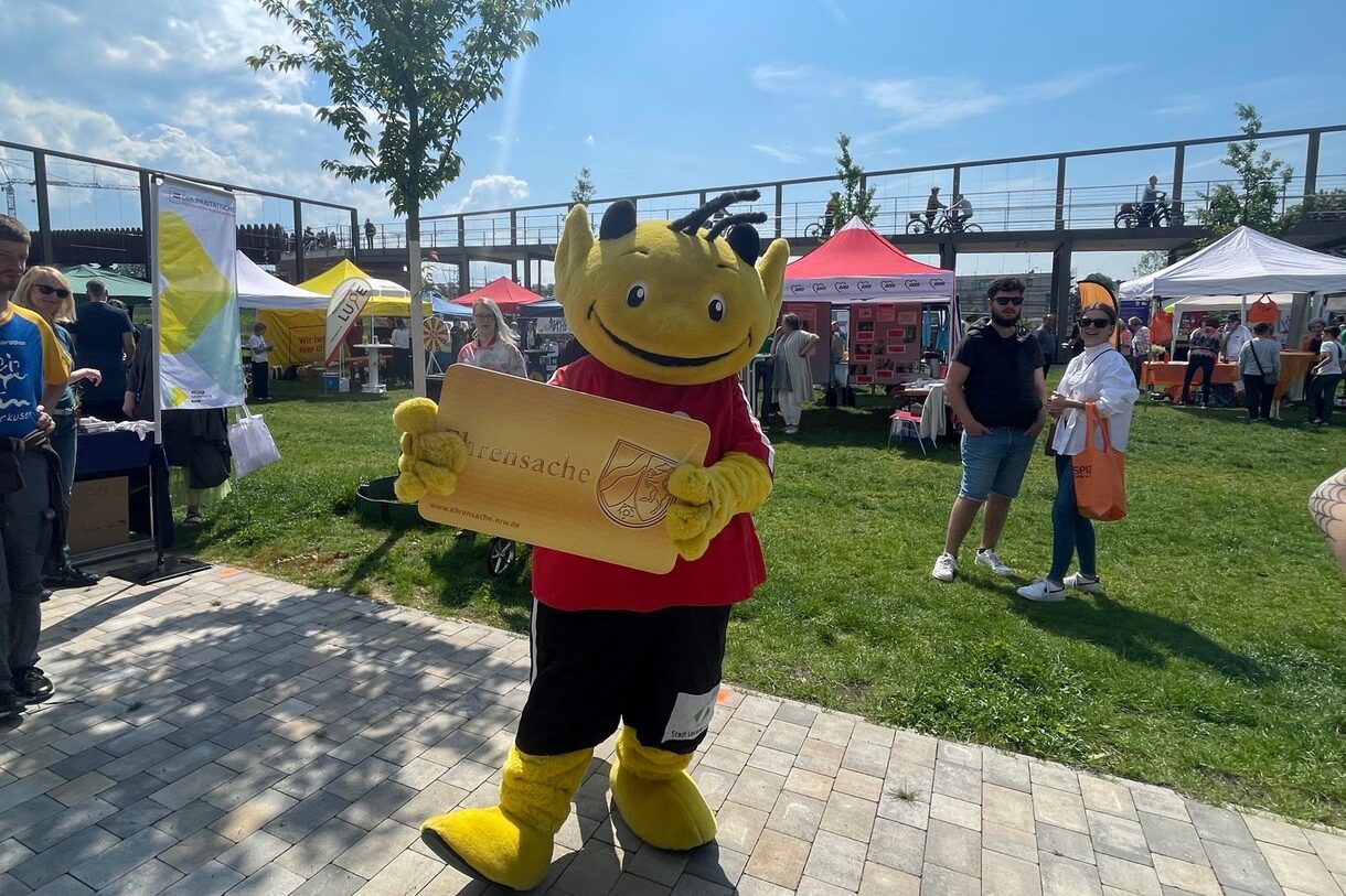 Maskottchen "Ehrenamtsteufel" hält die Ehrenamtskarte in den Händen