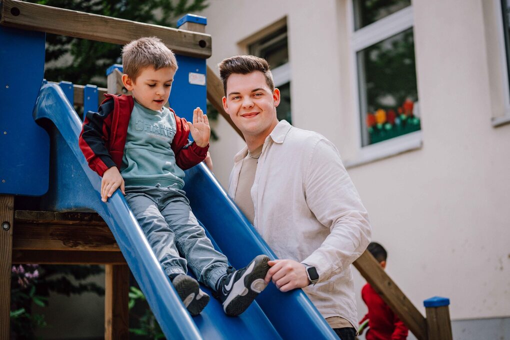Ein Kind rutscht von einer Rutsche, neben der ein Mann steht