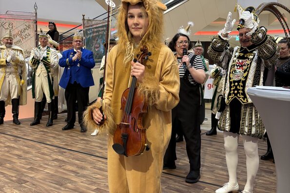 Ein Kind steht im Löwenkostüm auf der Bühne und hält eine Geige