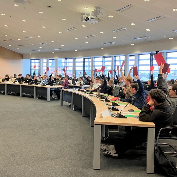 Jugendliche im Ratssaal heben rote Abstimmungskarten.