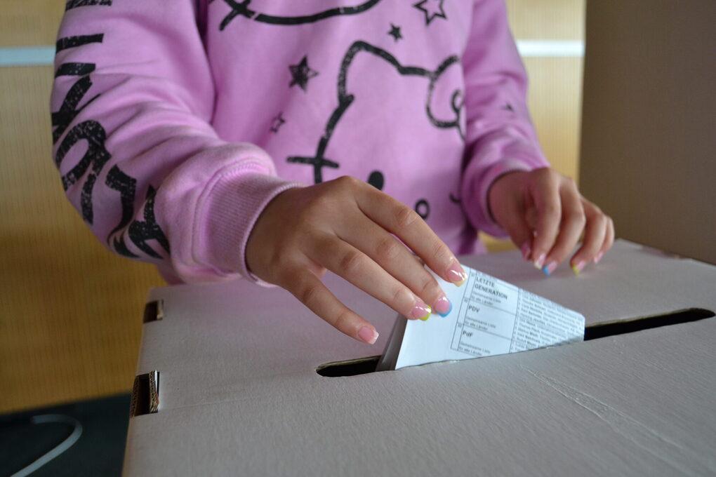 Hände eines Mädchens und Wahlurne mit Stimmzettel