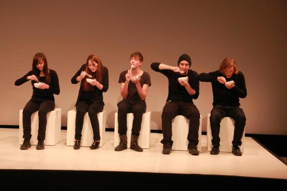 5 schwarzgekleidete Personen sitzen auf weißen Blöcken und essen