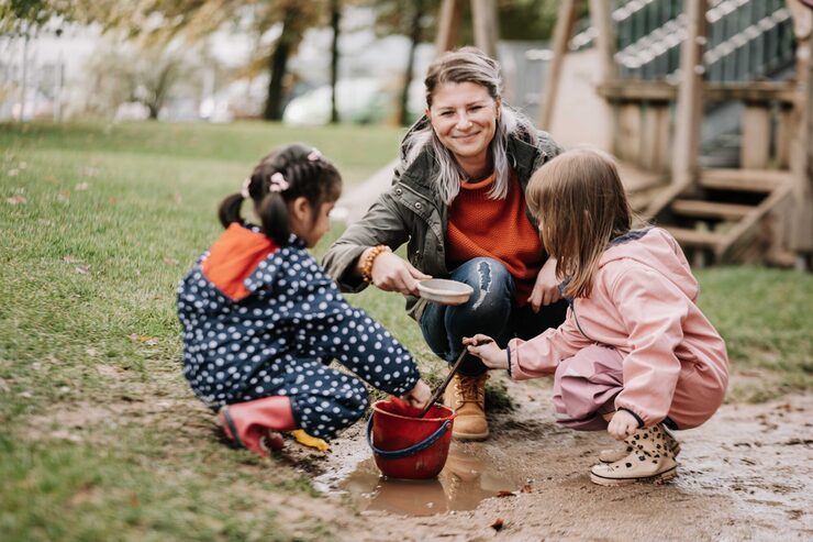 Frau sitzt mit zwei Kindern auf Spielplatz