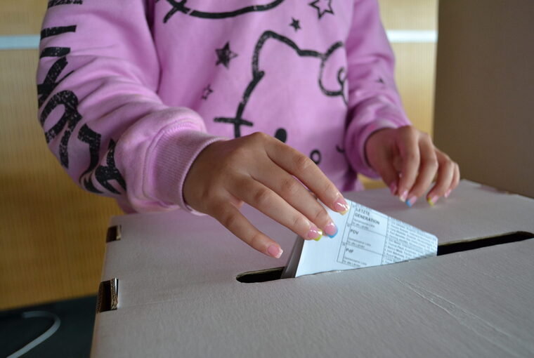 Hände eines Mädchens und Wahlurne mit Stimmzettel