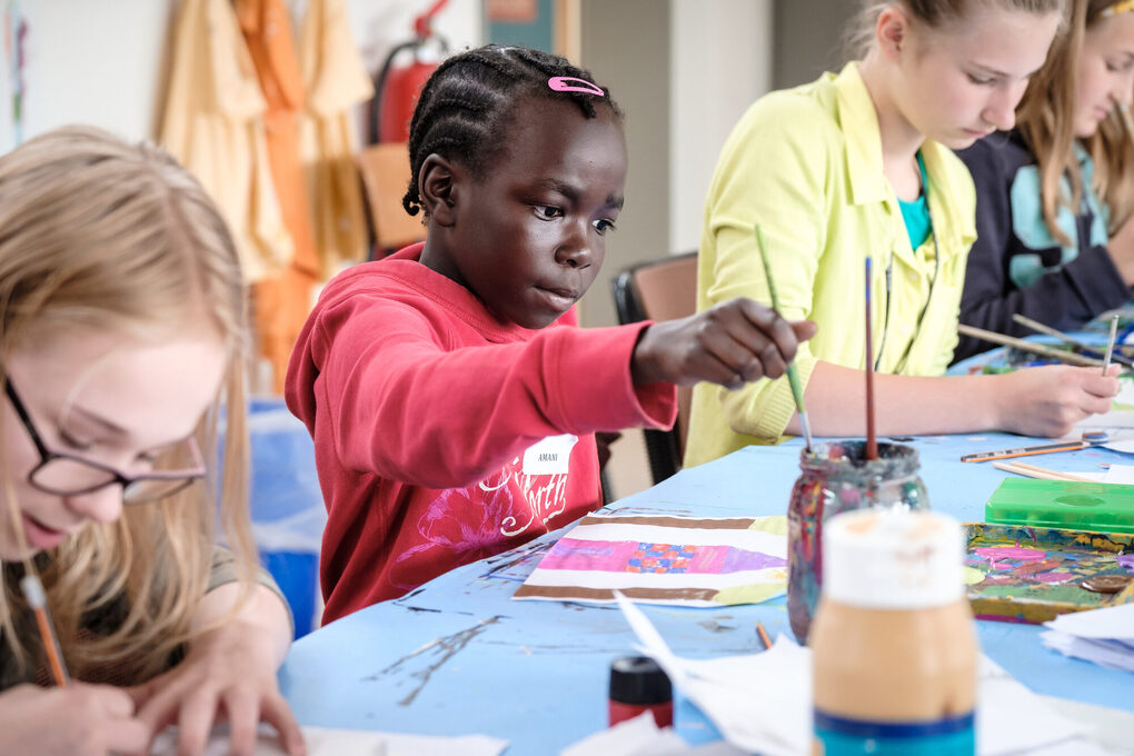 Kinder sitzen am Tisch und malen mit Wasserfarben