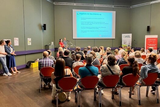 Viele Personen sitzen auf Stühlen vor der Präsentation zum Elternabend