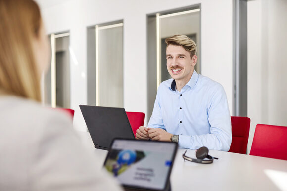 Ein Mann sitzt einer anderen Person lächelnd am Besprechungstisch gegenüber