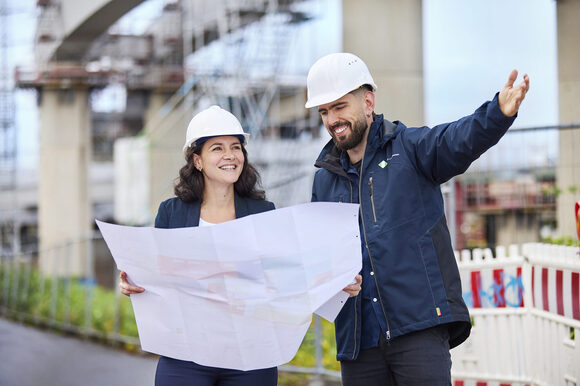 Zwei Personen sehen sich einen Bauplan an und lächeln