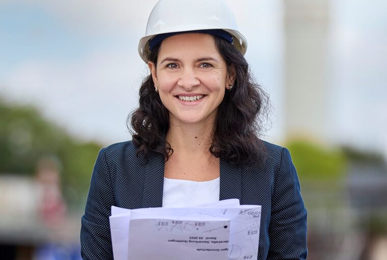 Eine Frau steht auf einer Baustelle und hält Baupläne in der Hand