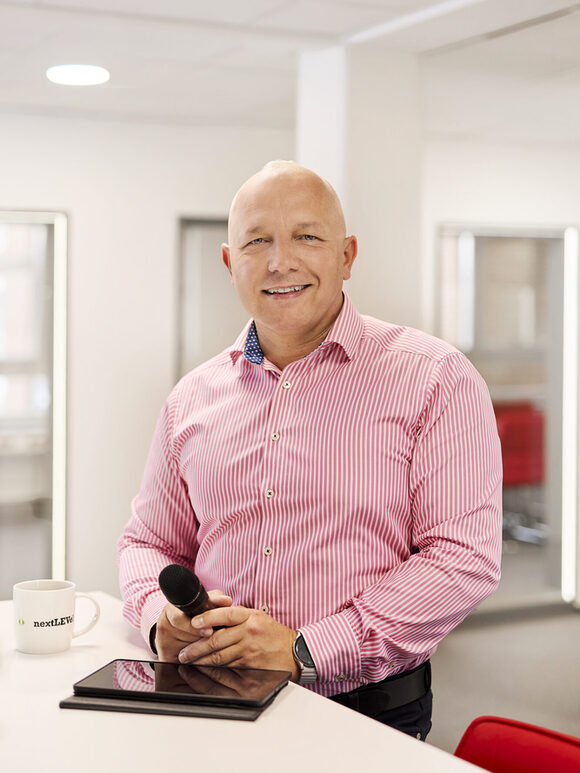 Ein Mann steht mit Tablet und Mikrofon am Schreibtisch