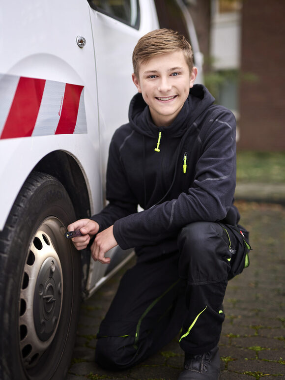 Ein junger Mitarbeiter der Stadt sitzt vorm Reifen eines Einsatzfahrzeuges