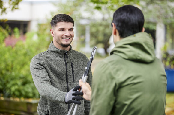 Ein Mann reicht einem anderen Mann eine Astschere