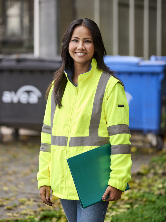 Eine Frau steht mit Warnjacke vor Mülltonnen