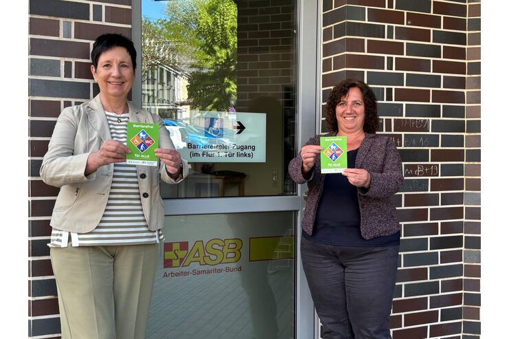 Zwei Personen stehen mit dem Gütesiegel Barrierefrei vor der ASB-Geschäftsstelle Leverkusen