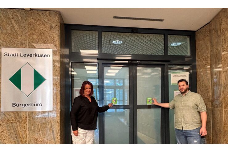 Zwei Personen stehen mit dem Gütesiegel Barrierefrei vor dem Bürgerbüro Leverkusen