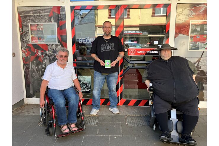 Drei Personen befinden sich vor dem Fanhaus Bayer 04
