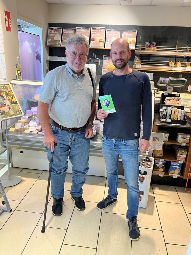 Zwei Personen stehen im Gut (Un)Verpackt Laden in Leverkusen mit Barrierefrei-Siegel in der Hand