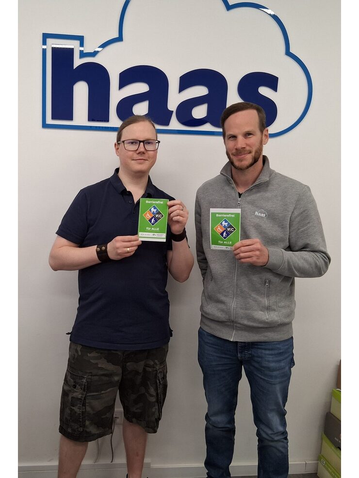 Zwei Personen stehen mit dem Gütesiegel Barrierefrei vor dem Haas Orthopädie-Schuhtechnik Logo