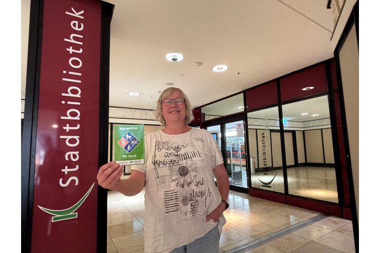 Eine Person steht mit dem Gütesiegel Barrierefrei vor der Stadtbibliothek Leverkusen