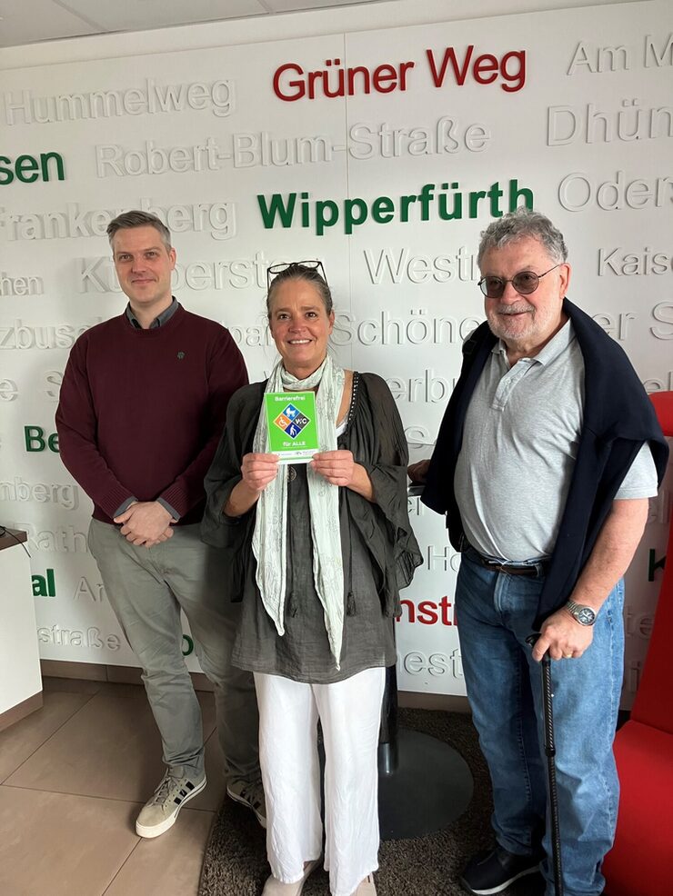 Drei Personen stehen mit dem Gütesiegel Barrierefrei vor dem wupsi Kundencenter in Fixheide